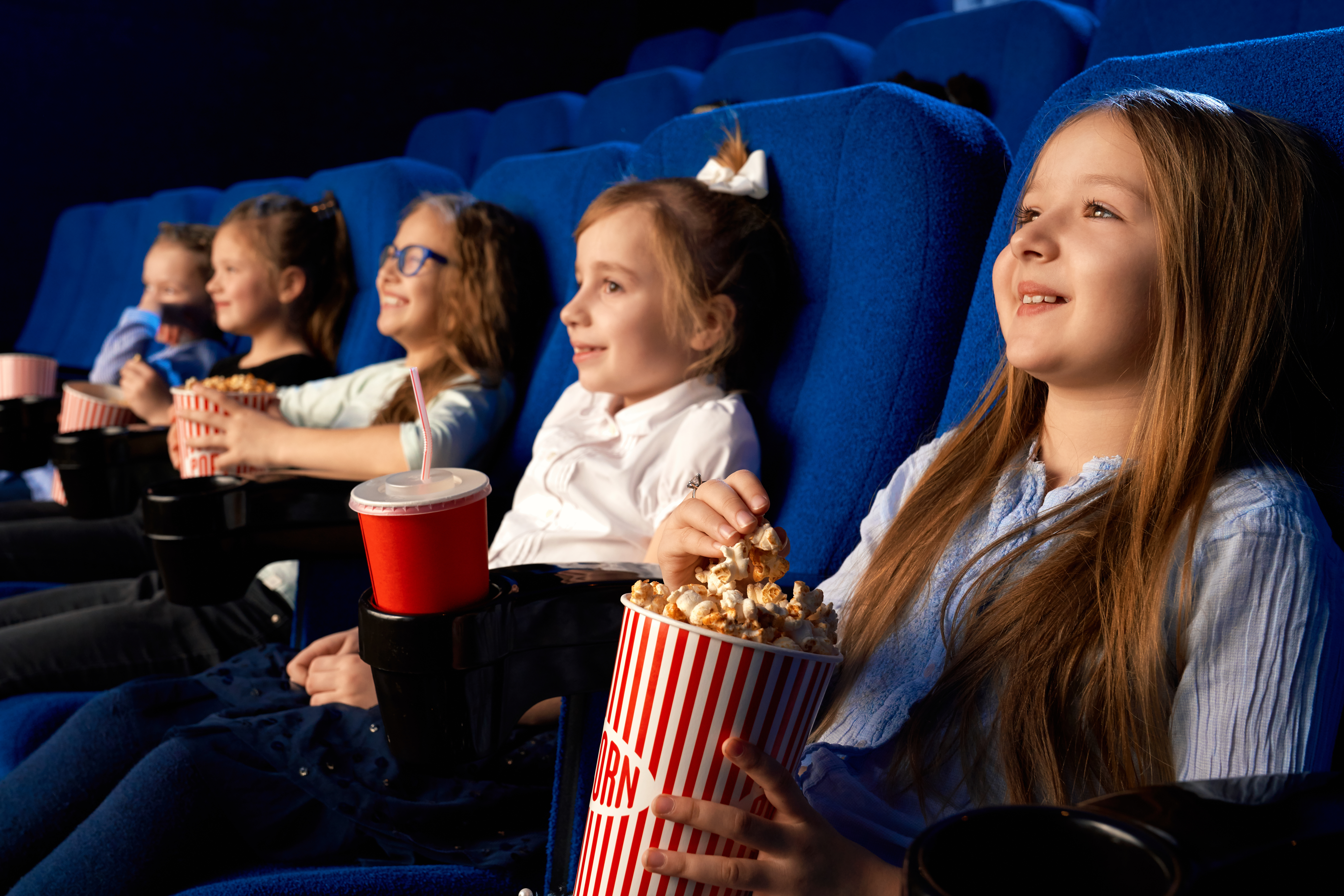 selective focus smiling little girl holding popcorn bucket sitting with laughing friends comfortable chairs cinema children watching cartoon movie enjoying time 1 Семь виртуальных концертных зала открыли в Мордовии